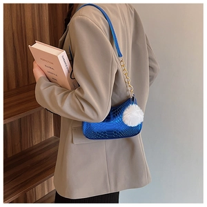 Detail of blue faux-crocodile leather shoulder bag with gold chain and white fluffy charm