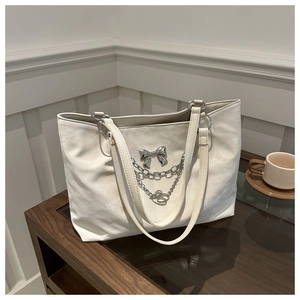 Détail d'un sac cabas crème avec boucle papillon argentée et bandoulière en chaîne métal