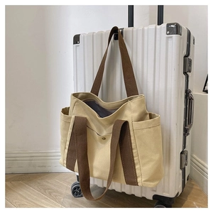 Detail of canvas tote bag on luggage handle showing side pocket and durable brown strap