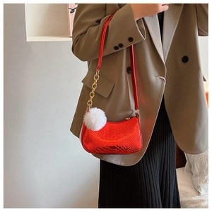 Detail of red faux snake pattern crescent bag with golden chain and white pompom charm