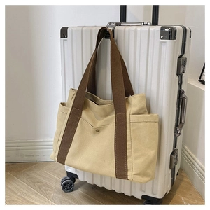 Close-up of beige canvas tote bag with brown straps hanging on a white suitcase