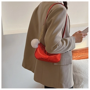 Detail of red snake-patterned hobo bag with gold chain and white plush charm accessory