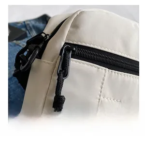Close-up of smooth black zipper and high-density nylon fabric on off-white crossbody bag