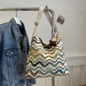 Detail of colorful wave knit tote bag featuring wide geometric strap and plush monster charm