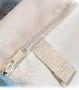 Close-up of the smooth matching lacquer zipper and twill fabric texture on the off-white bag