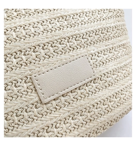 Détail de la texture en paille tressée crème et du patch en cuir sur le sac à bandoulière