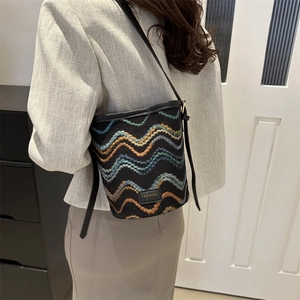 Detail view of woven bucket bag with wave patterns and black leather shoulder strap