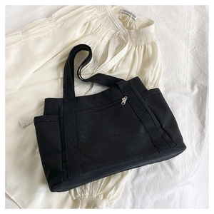 Detail of black canvas tote bag with front zipper pocket and side pockets on white shirt