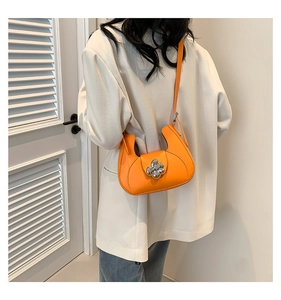 Détail d'un sac hobo orange vif avec fermoir fleur argentée sur une veste blanche