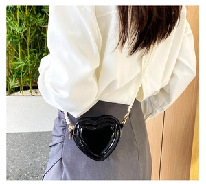 Detalle de bolso negro de corazón con cadena de perlas y acabado brillante de moda