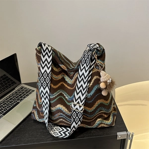 Detail of colorful wavy knit tote bag with geometric strap and plush pendant on wood desk