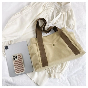 Detail view of khaki canvas tote bag featuring front snap pocket and reinforced brown handles