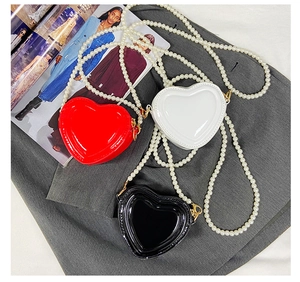 Detalle de minibolsos de corazón brillantes en rojo, blanco y negro con asa de perlas