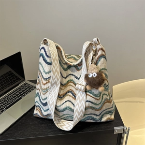 Close-up of bohemian striped knit tote bag with brown plush monster charm on desk