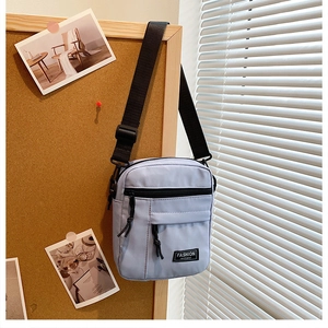 Detail view of light blue nylon crossbody bag featuring a woven zip pull and brand label