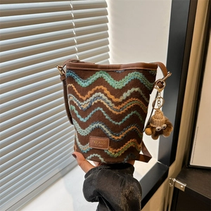 Detail of knitted bucket bag with colorful wavy patterns and cute monster plush pendant
