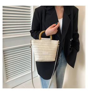 Détail d'un sac seau en paille tressée avec poignée en bois et bandoulière en cuir