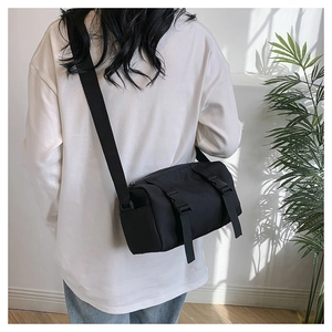 Rear view of model wearing black cylindrical crossbody bag with adjustable wide strap