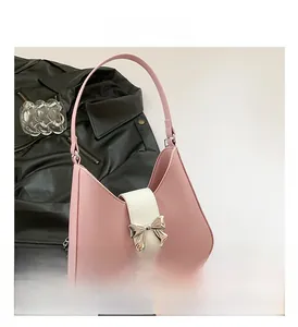 Close-up of pink saddle bag with white flap and golden metal bow detail on a leather background