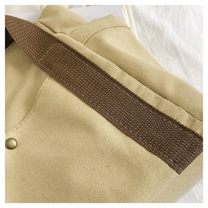 Detail of khaki canvas fabric with brown woven strap and circular metal button closure