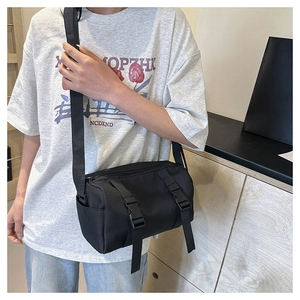 Detail of black cylindrical crossbody bag featuring double buckle nylon strap accents