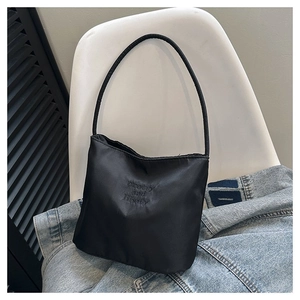 Detail of black nylon shoulder bag with embroidered text placed on a blue denim jacket