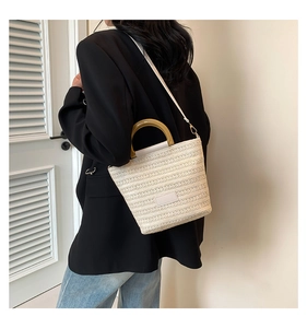 Détail du sac tissé crème avec poignées en bois sur un mannequin en blazer noir