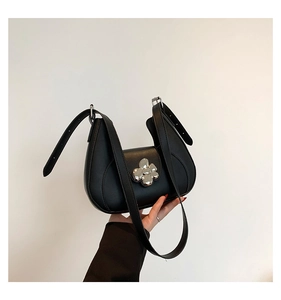 Détail du sac sous le bras en cuir noir avec une grande boucle métallique en forme de fleur argent