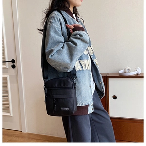 Vertical black nylon crossbody phone bag shown with adjustable strap on a street style outfit