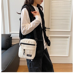 Detailed shot of an adjustable strap and front pocket on the off-white canvas crossbody bag