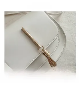 Close-up of golden metal decorative hardware and tassel detail on white leather crossbody bag