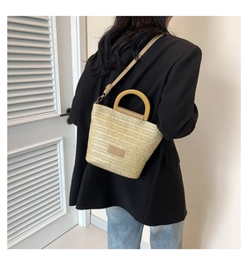 Détail d'un sac seau en paille tressée avec poignées rondes et bandoulière en cuir