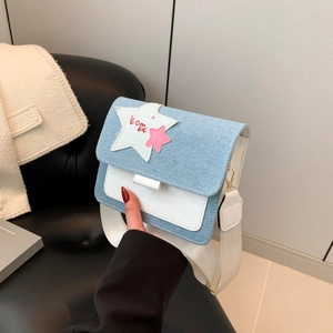 Denim patchwork crossbody bag with star applique and wide strap held in hand