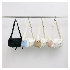 Detail of four cylindrical canvas crossbody bags in black, blue, brown, and pink colorways