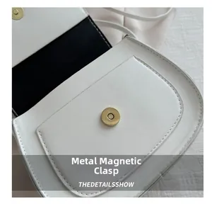 Detail of the golden magnetic hardware clasp on a white leather shoulder bag