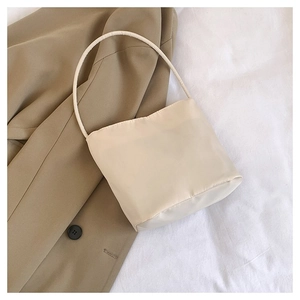 Close-up of cream nylon minimalist baguette bag with slim shoulder strap on soft fabric
