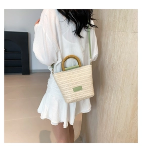 Détail du sac seau en paille tressée avec bordure en cuir vert et anses en bois