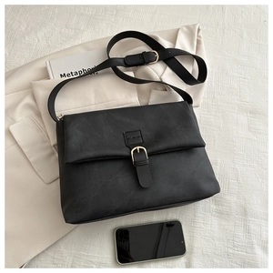 Détail du sac noir mat vintage avec boucle dorée sur fond de veste de tailleur blanche