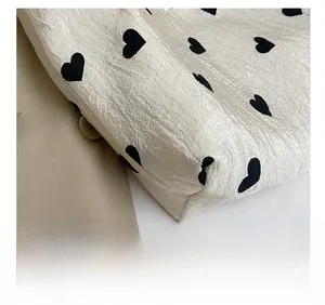 Detailed close-up of precise stitching and black heart patterns on a beige tote bag
