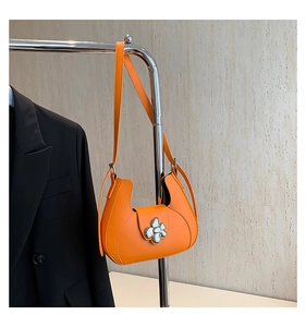 Détail du sac hobo orange vif avec boucle florale argentée et texture en cuir élégante