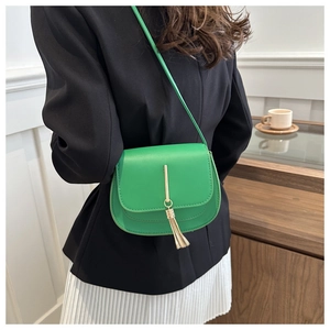 Detail of green mini crossbody bag featuring golden metal bar and elegant fringe tassel