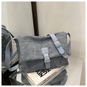 Détail du sac en toile bleu-gris avec bandoulière en cuir et boucle sur des livres