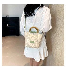 Détail d'un sac cabas en paille tissée avec finitions cuir vert et poignées en bois rondes