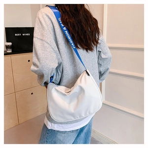 Detail of white crescent crossbody bag with a contrasting blue fashion strap worn by model
