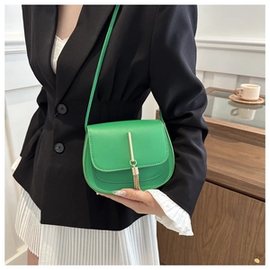 Detail of green leather saddle bag featuring gold metal bar and elegant fringe tassel