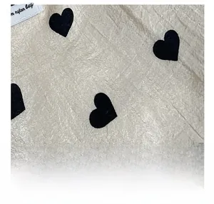 Close-up of textured beige canvas fabric with black heart patterns and stitched label