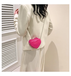Detail of bright pink heart-shaped crossbody bag with silver chain on model in white blazer