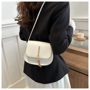 Detail of white saddle bag with gold tassel pendant worn by model in a cozy cafe setting
