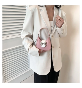 Pink and white saddle bag with silver bow accent carried by model in white suit