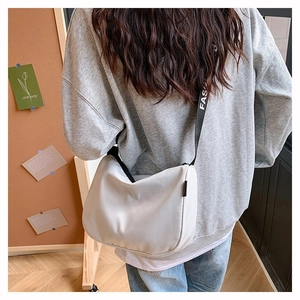 Close-up of a white canvas moon bag featuring a wide black alphabet shoulder strap